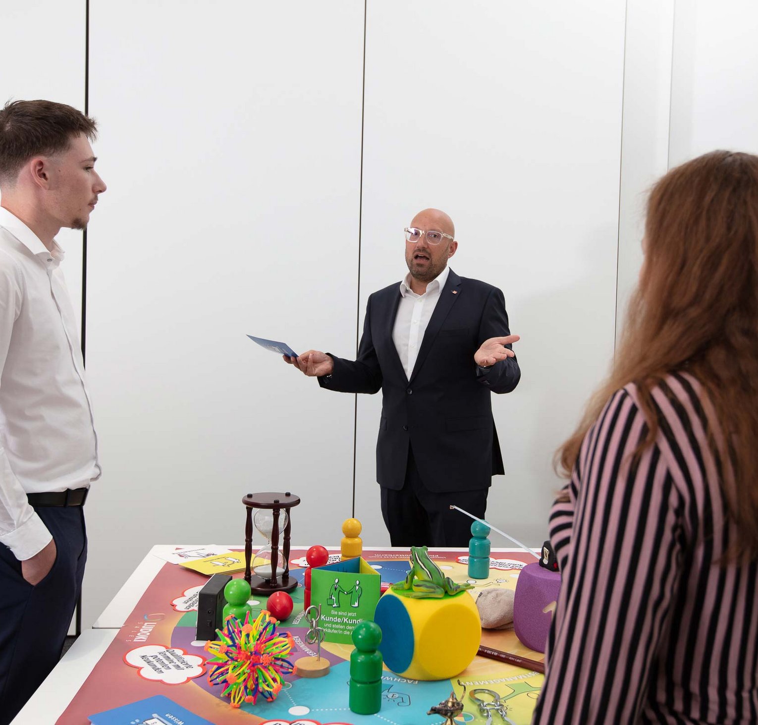 Sales seminars in Gotterbarm Three people are engaged in a discussion around a table filled with colorful toys and educational materials, suggesting a brainstorming or planning session in a professional setting.